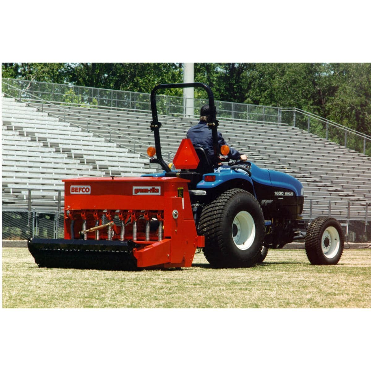 BEFCO Green-Rite Seeder and Aerator in red, side view, mounted on a blue tractor.