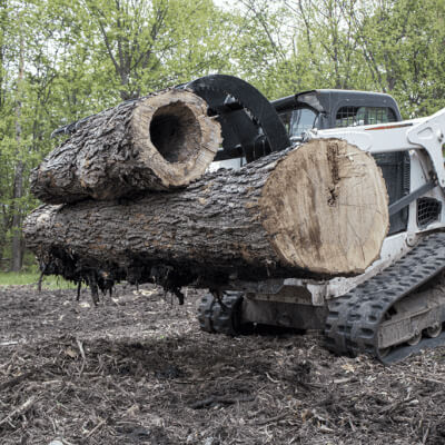 Clamshell Grapple for Skid Steer by Prime Attachments, black, angled view, holding large logs.