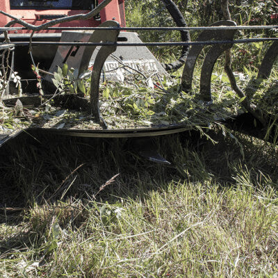 Skid Steer Mower Attachment by Prime Attachments, angled view, featuring curved blades and grass clippings.
