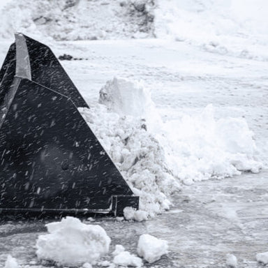 Prime Attachments Skid Steer Snow Bucket, black, angled view with snow accumulation.