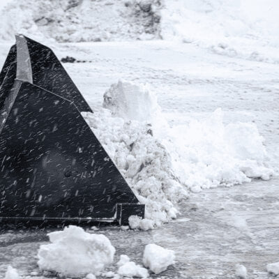 Prime Attachments Skid Steer Snow Bucket, black, angled view with snow accumulation.