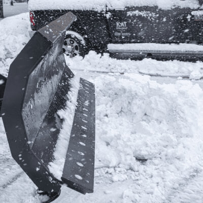 Skid Steer Snow Plow Blade by Prime Attachments, angled view, black with snow accumulation.