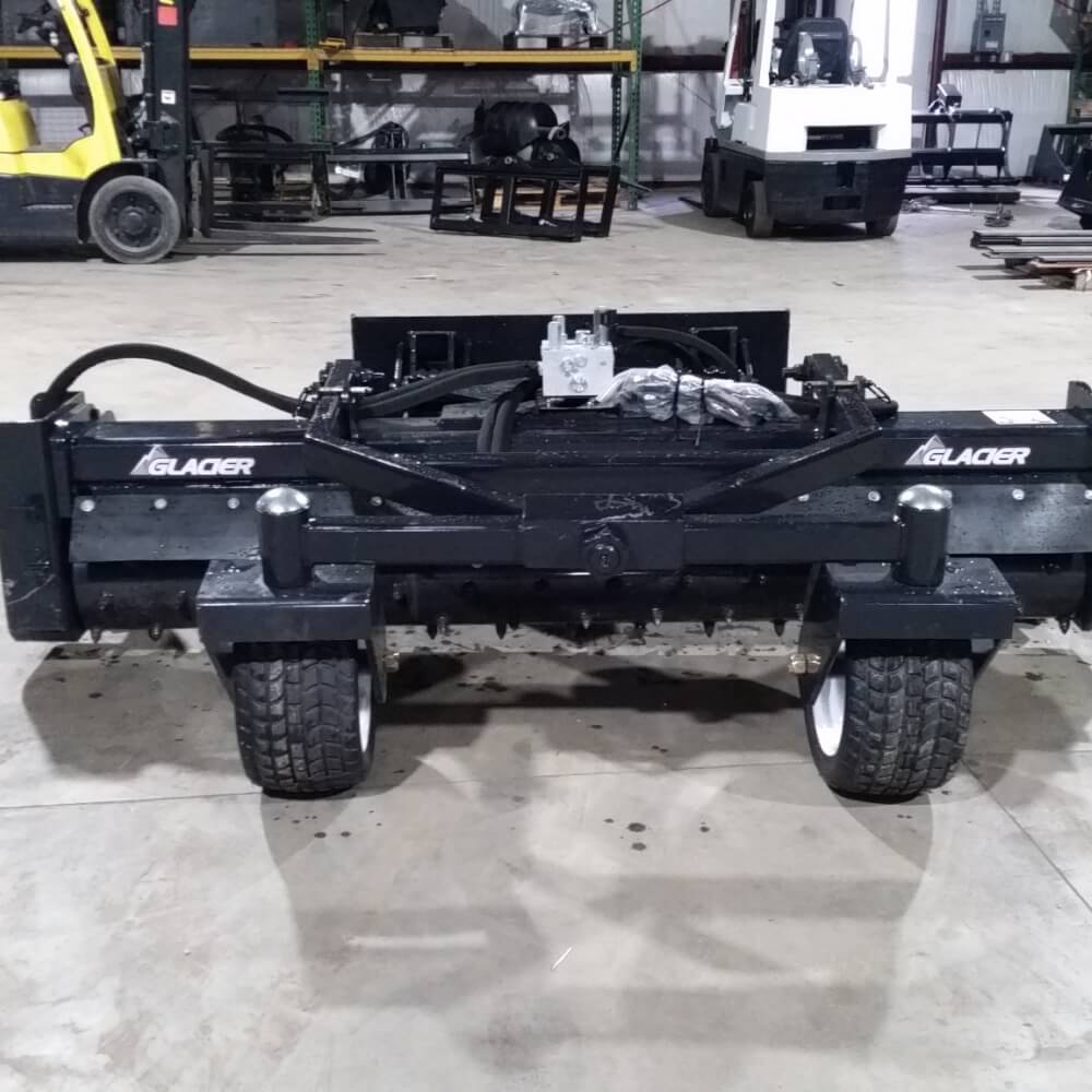 Glacier Attachments Skid Steer Soil Conditioner front view, black with wheels and hydraulic components.