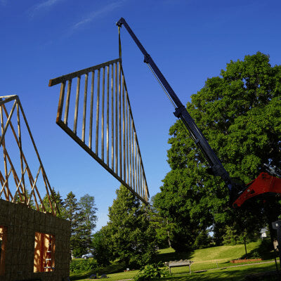 Skid Steer Teleboom by Prime Attachments in action, lifting building materials at a construction site.