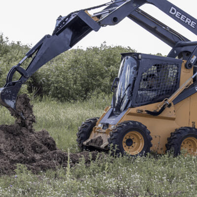 Backhoe for Skid Steer — Prime Attachments, angled view, black with yellow accents, digging into soil.