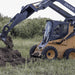 Backhoe for Skid Steer — Prime Attachments, angled view, black with yellow accents, digging into soil.