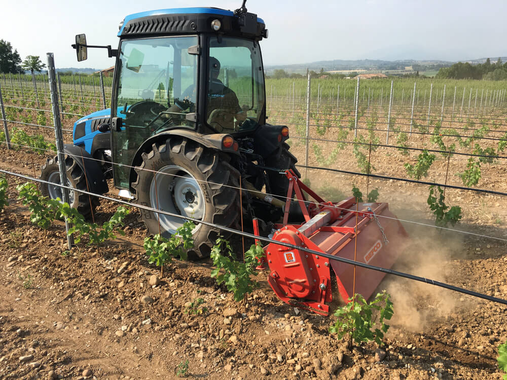 BEFCO T50 Rotary Tiller in red, attached to a tractor, working in a vineyard.