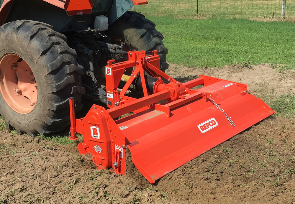 BEFCO T70 Rotary Tiller in vibrant orange, angled view with connected tractor and tilling blades.