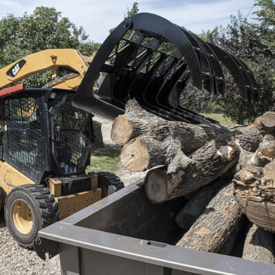 Forestry Grapple for Skid Steer by Prime Attachments, black, angled view, gripping logs.