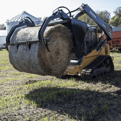 High Capacity Grapple Bucket by Prime Attachments, black, angled view, gripping large round hay bale.