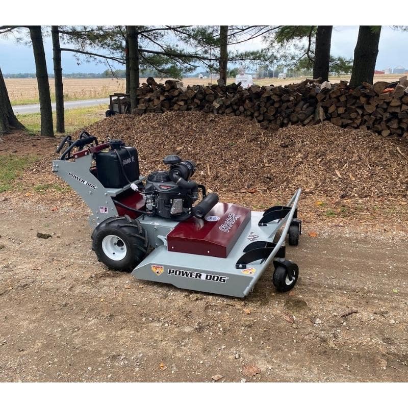 Power Dog commercial brush mower parked near woodpile, side view of heavy-duty field mower.