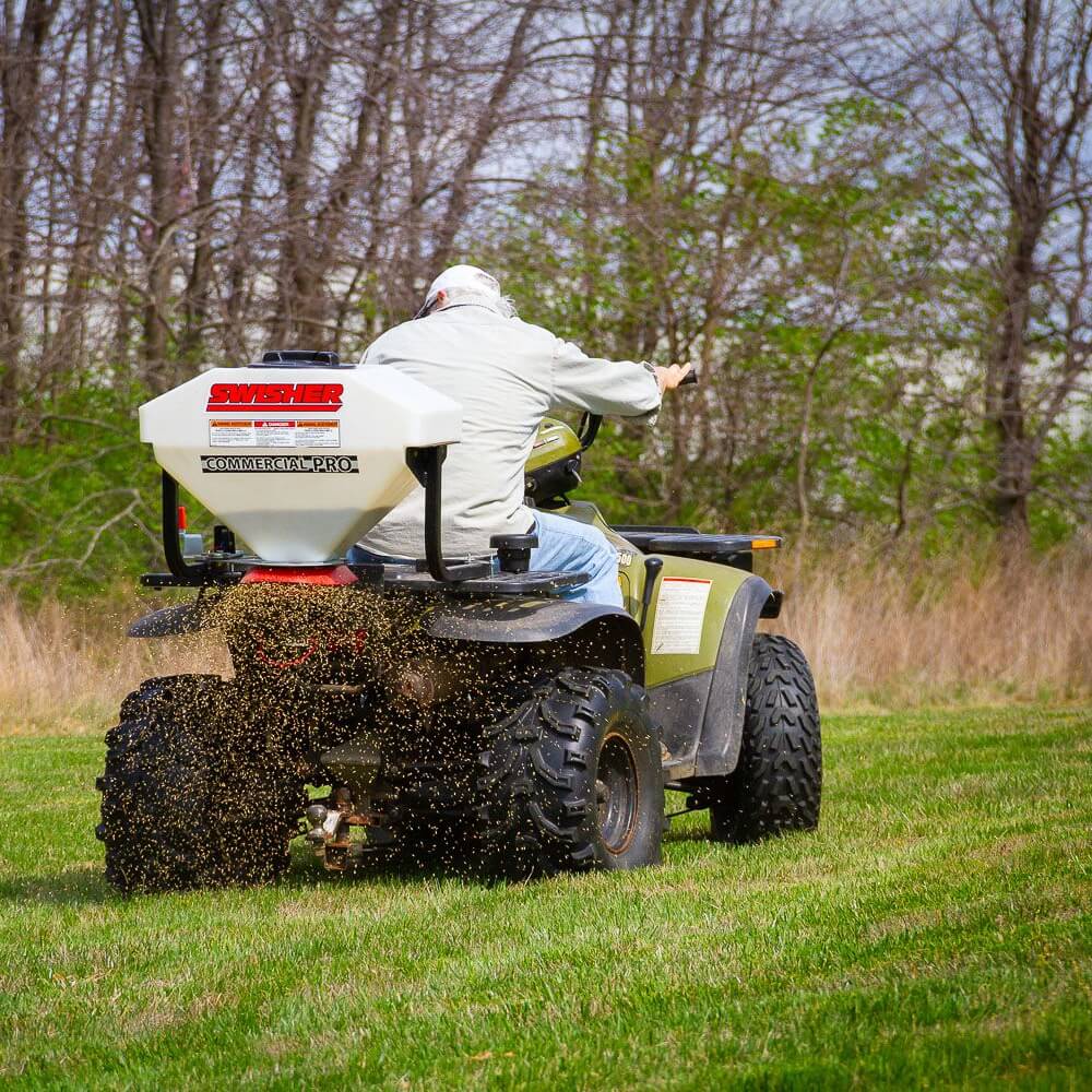 Swisher Commercial Pro ATV Spreader, rear view with white hopper and spreading feature in action.