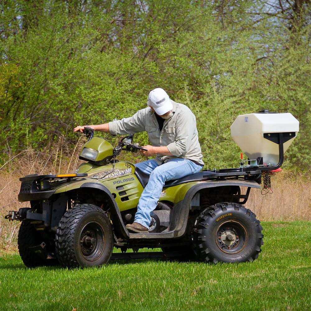 Swisher Commercial Pro ATV Spreader mounted on an ATV, featuring a white hopper and black wheels.