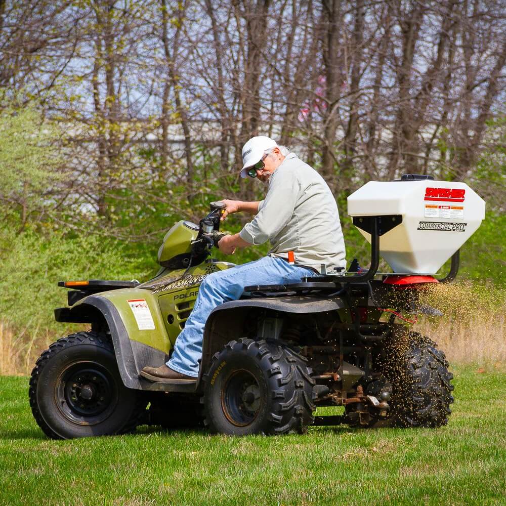 Swisher Commercial Pro ATV Spreader, white hopper, mounted on ATV, dispersing material.